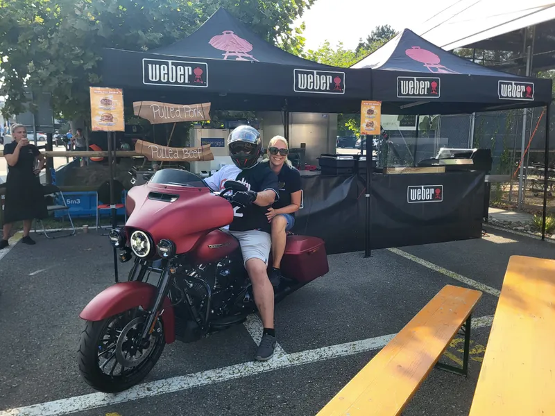 Gäste auf einem Motorrad vor dem NNBS Weber-Smoker-Stand mit Pulled-Pork-Burgern