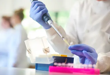 Laboratory technician performing liquid handling procedures during assay development and reagent testing.