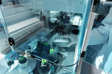 Laboratory automation system handling microplates and sample tubes inside an enclosed workstation, with a gloved technician loading samples for high-throughput nucleic acid therapeutics research and development.