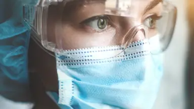 Laboratory worker wearing personal protective equipment, including safety goggles and a face mask, in a controlled research environment.