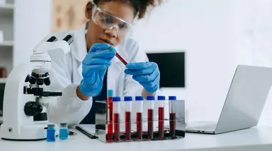 Laboratory professional examining a blood sample alongside diagnostic testing equipment, representing laboratory analysis, quality management and accurate patient testing.