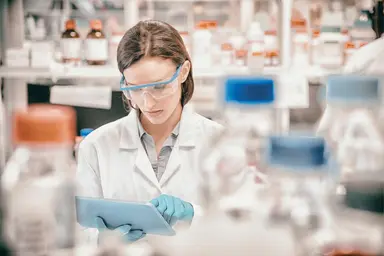 Laboratory professional using a tablet in a laboratory environment, representing diagnostic quality management, testing oversight, data review and quality assurance processes.