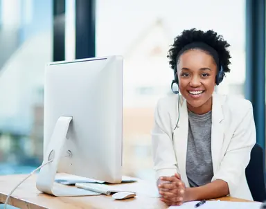 Customer support representative wearing a headset at a computer in an office.