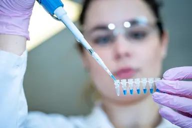 Laboratory scientist using a pipette to dispense liquid into a strip of microtubes, supporting assay validation, reference material preparation and quality assurance in molecular and next-generation sequencing workflows.