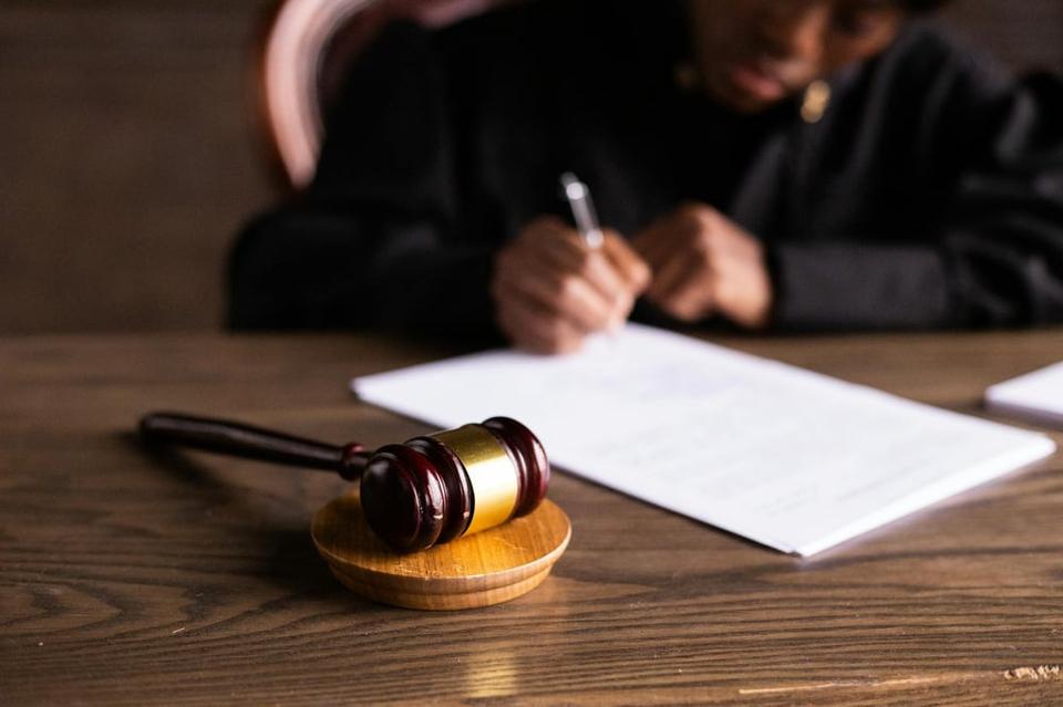 A gavel rests on a block and in the background, a judge signs a piece of paper.