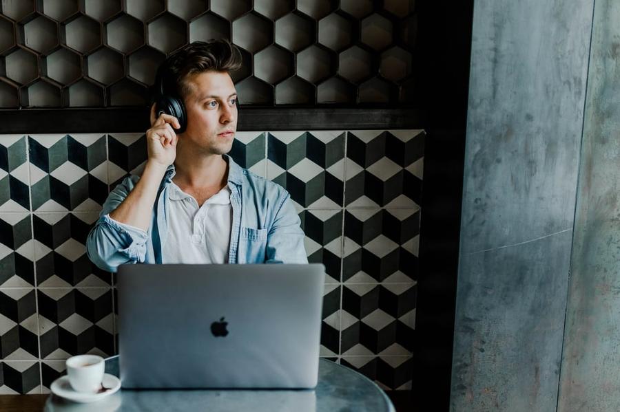 A man in a coffee shop sitting behind his laptop while on the phone.