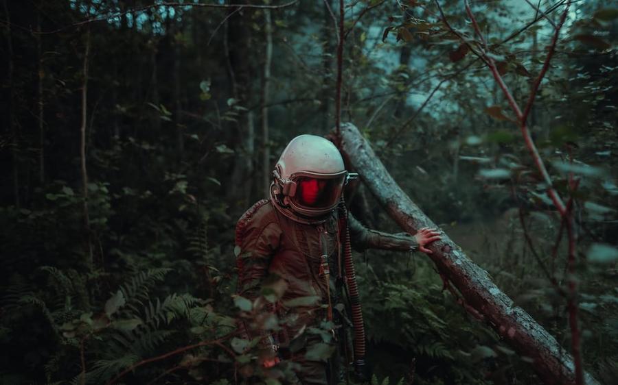 Woman in an astronaut's suit wandering through a dark forest.