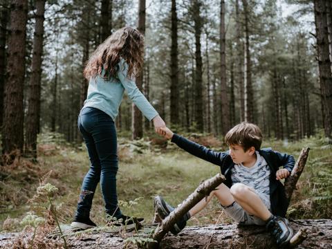 One child helping another up while standing on a fallen log.