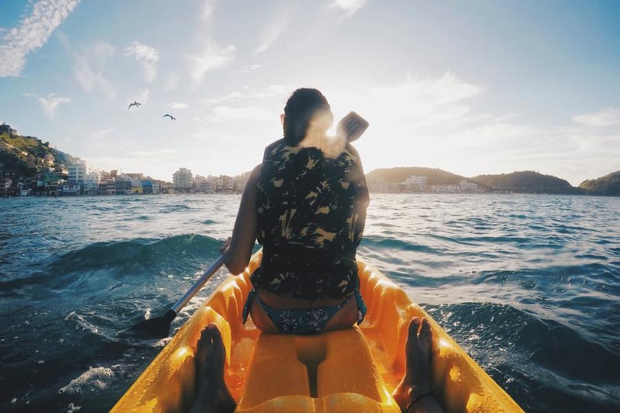 A view from behind a person sitting in the front of a canoe on open water.