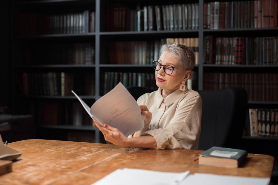 An older writer sits at a desk reviewing a manuscript.