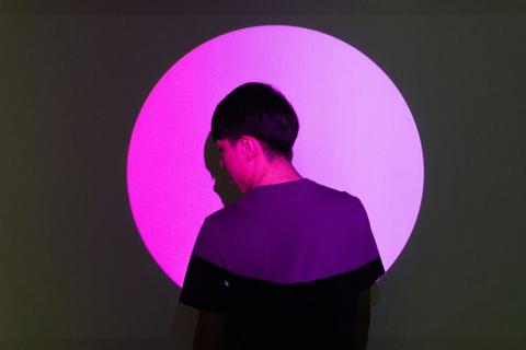 A person standing in a round purple spotlight.