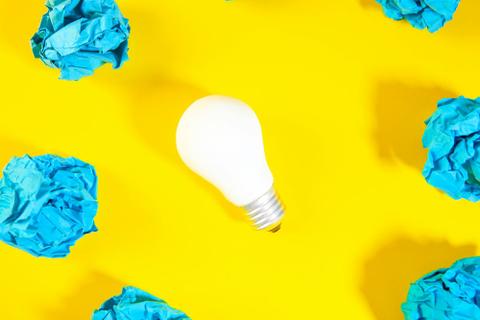 A white lightbulb surrounded by wads of blue paper on a bright yellow background.