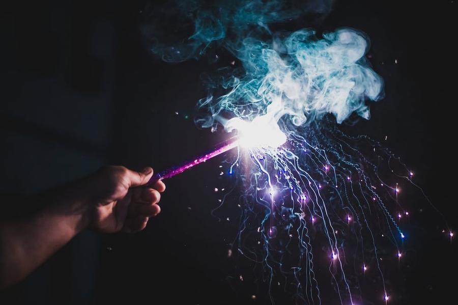 Person showing glowing sparkler against night sky.