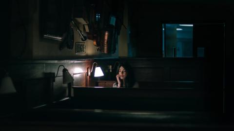 A woman sitting next to a light in a dark and empty restaurant.