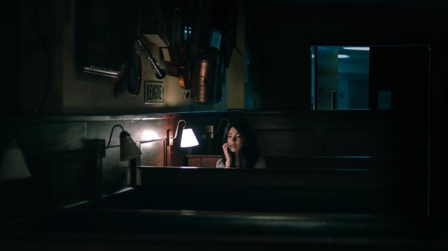 A woman sitting next to a light in a dark and empty restaurant.