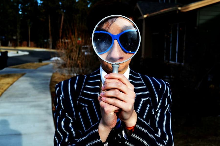 Person in a striped jacket holding a large magnifying glass in front of their face to enlarge their eyes and nose.