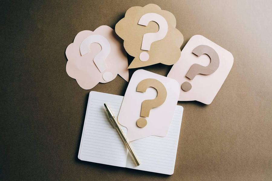 Four construction paper question marks above an open notebook and a gold pen.
