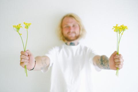 A blond Nice Guy type holds out two fists of yellow flowers.