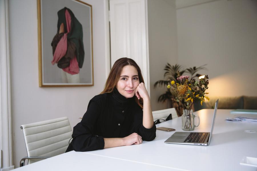 An author sits in front of a computer in a clean, white room and smiles at the camera.