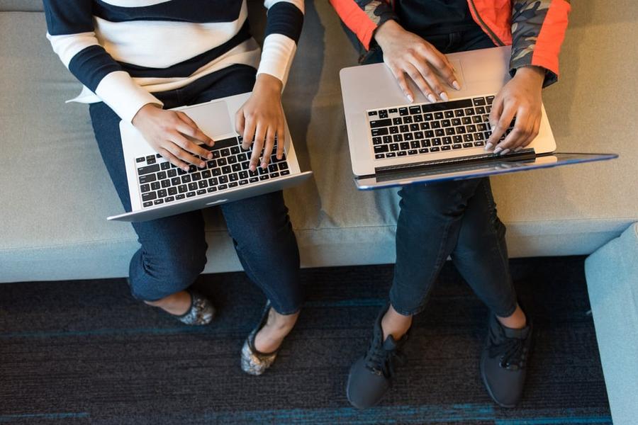 Overhead view of two laptops sitting on the laps of two writers.