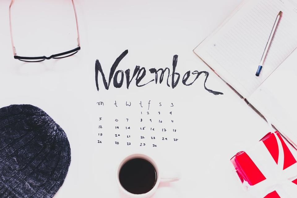 A calendar page reading "November" surrounded by writing supplies and a cup of coffee.