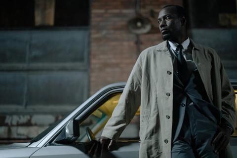 A detective stands outside his car at night.