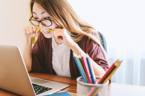 A nervous person bites a pencil as they look at a computer screen.