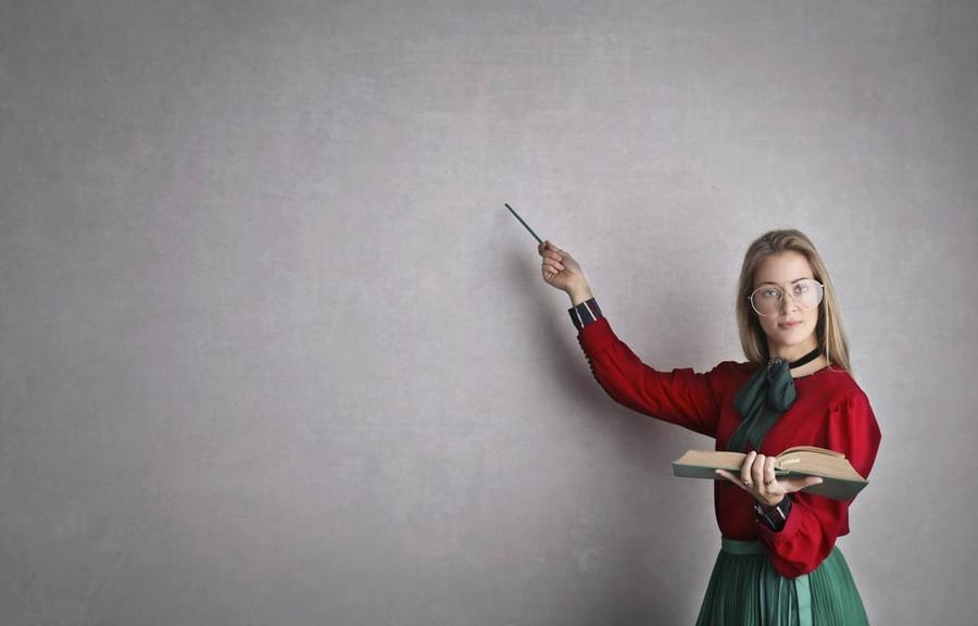 A woman with a book in one hand and a stick in the other, using the stick to point at the wall.