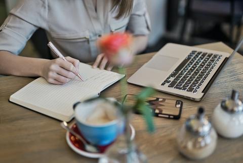 Woman Sitting on Gray Chair While Writing on Table