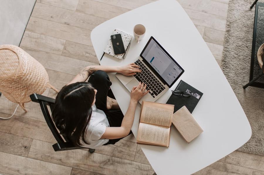 A woman sitting at a desk, typing on a laptop with books around her.