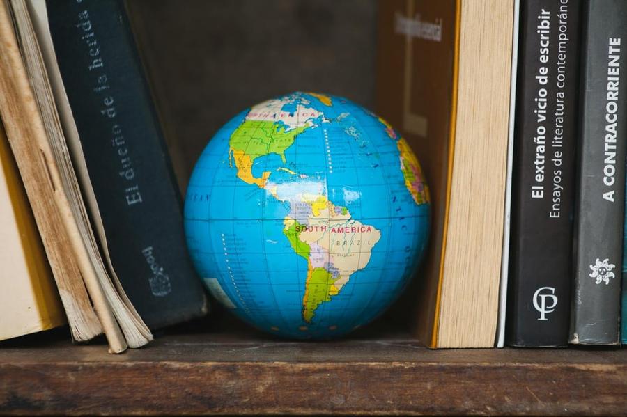 A globe sits between books on a bookshelf.