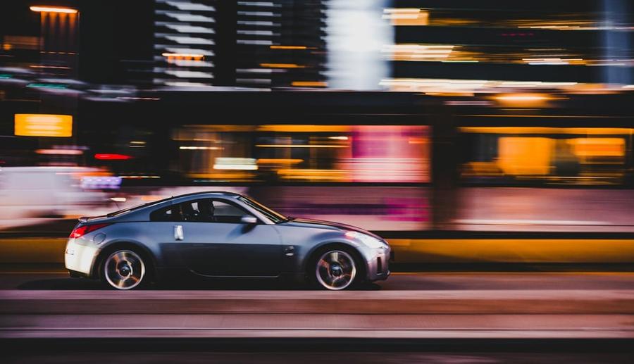 Silver sports car driving quickly by streaks of neon light.