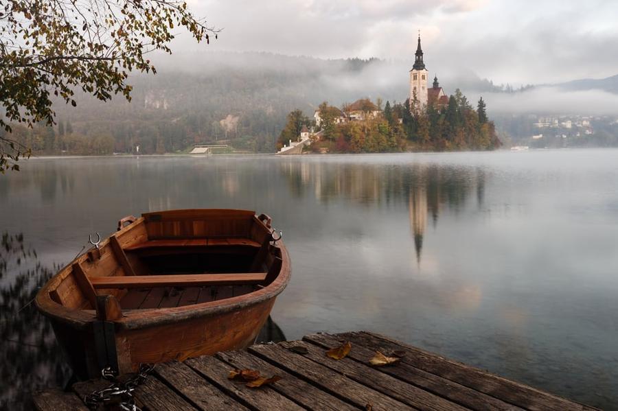 A wooden boat sits on a lake, opposite a shore that holds the castle of a fantasy world.
