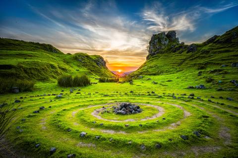 A grassy valley between mountains with the sun rising on the horizon.