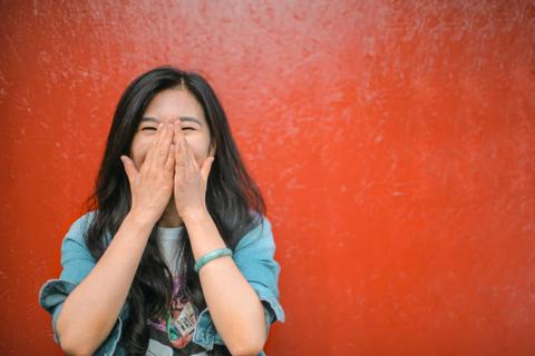 A person smiles with their hands over their mouth.
