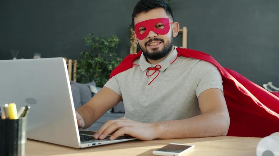A person in a mask and cape sits at a computer.