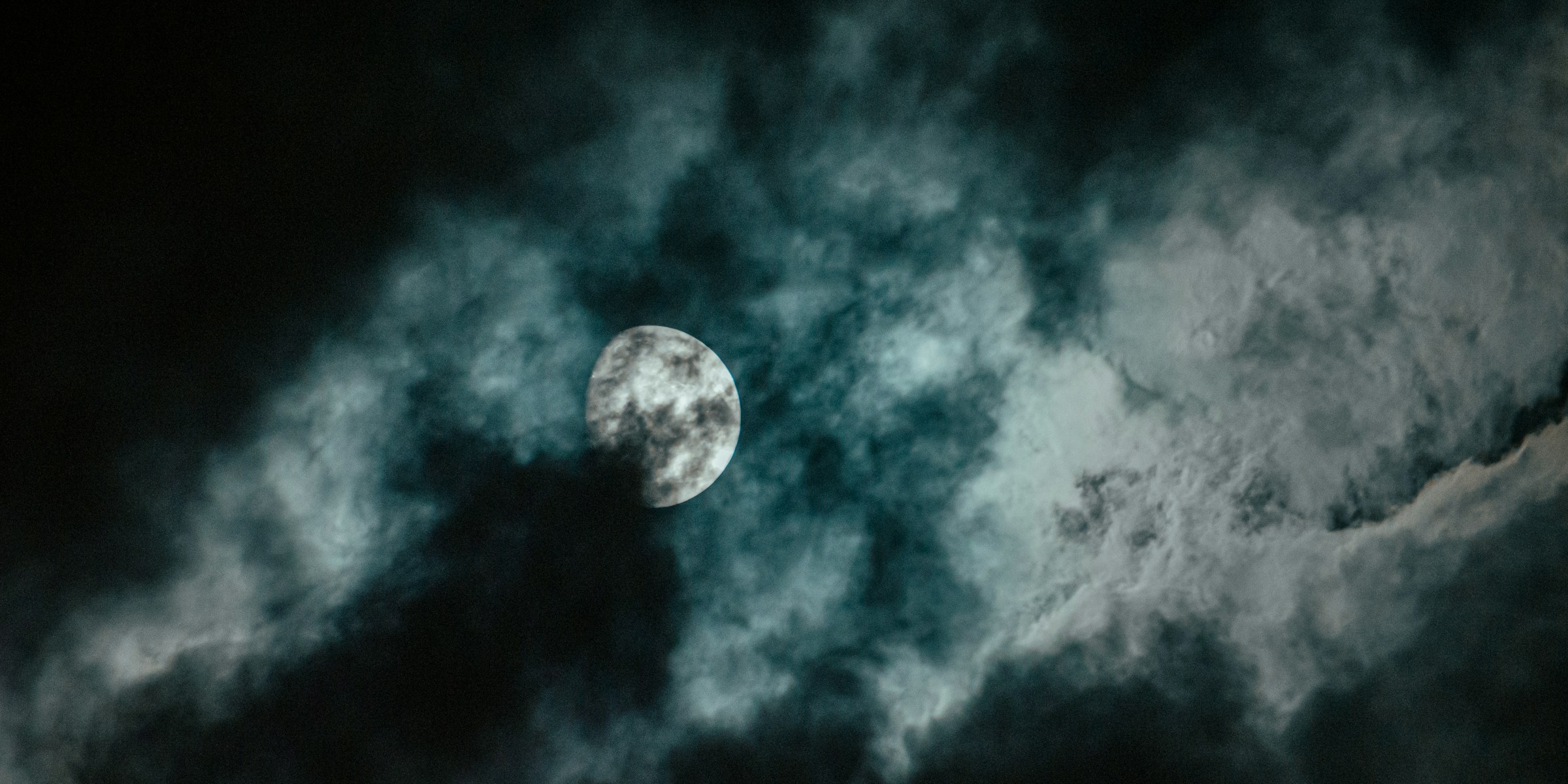 A bright white moon peering out from between dark clouds.