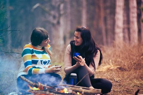 Two women sitting in the woods, speaking to one another.