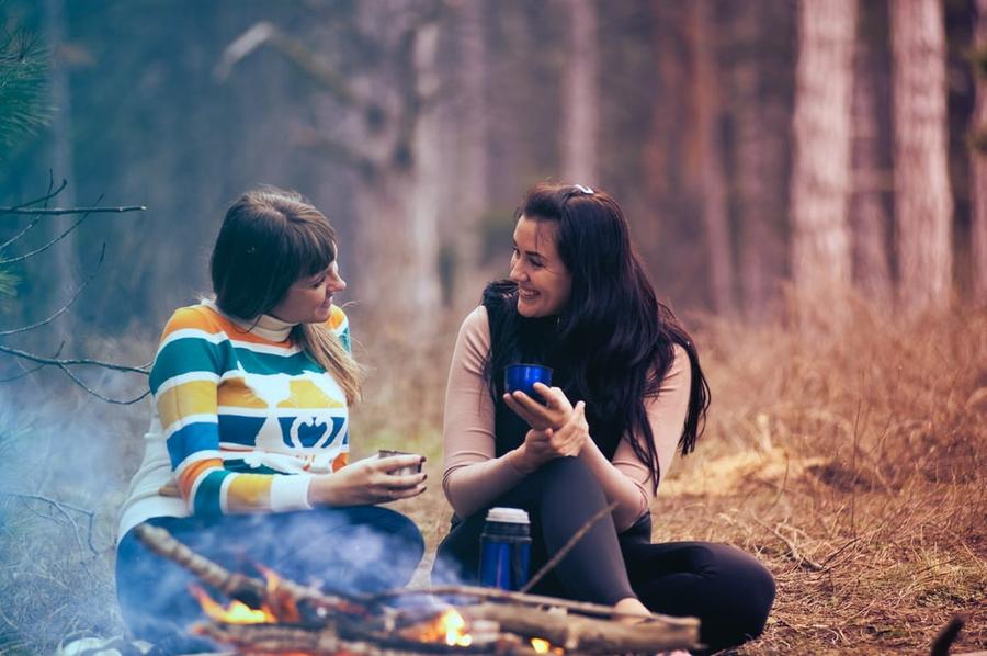 Two women sitting in the woods, speaking to one another.