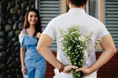 A "nice guy" holds a bouquet of flowers behind his back as a woman approaches.