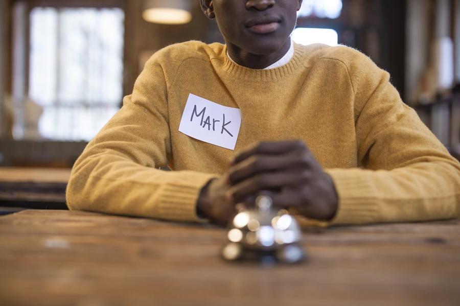 A person sits at a table in front of a bell wearing a name tag that says "Mark."
