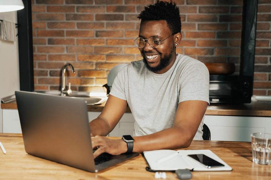 A smiling person types a query letter on a laptop in a brick-walled kitchen.