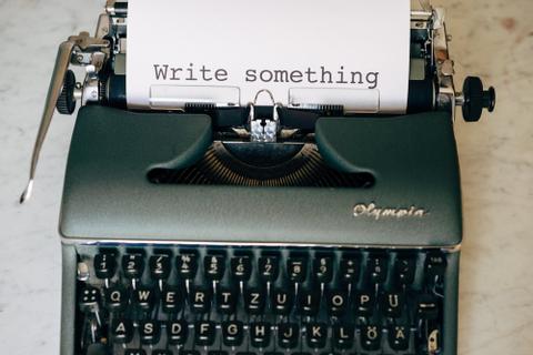 Green typewriter with a page sticking out of it with "Write Something" typed on the page.
