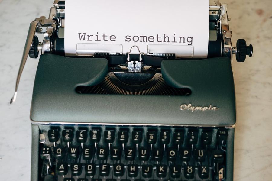 Green typewriter with a page sticking out of it with "Write Something" typed on the page.