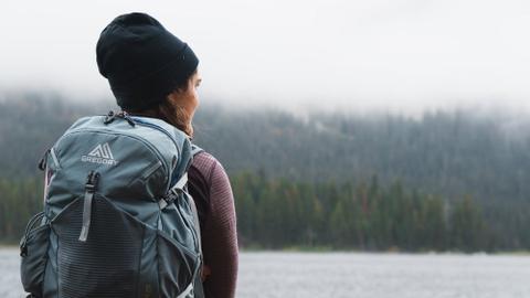 A person carrying a backpack looks out over snow-covered wilderness.