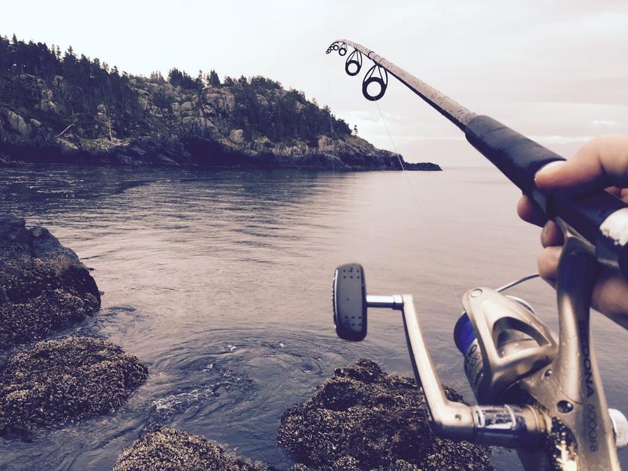 First-person perspective of a person casting a fishing line from a rocky shore.