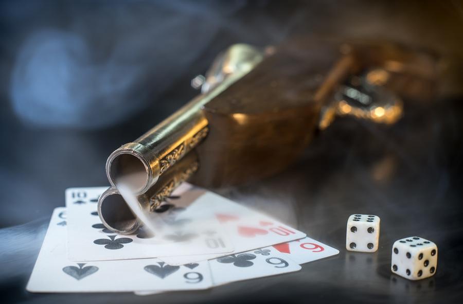 A vintage gun on a table with playing cards and dice. Smoke is spilling from the barrel of the gun.