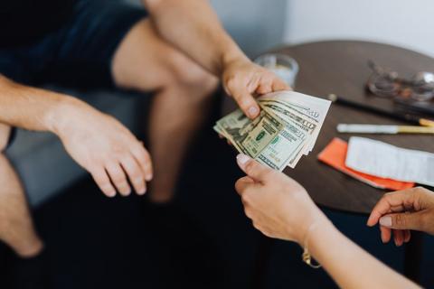 The arms of two people who are sitting around a small coffee table. They are exchanging a variety of US dollar bills.