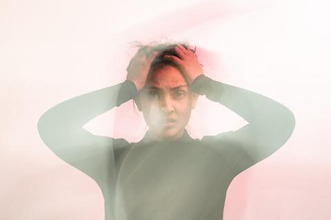 Blurred image of woman in gray turtleneck, grabbing her hair in stress.