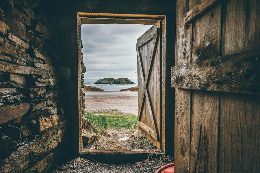 A barn door opens to reveal a beautiful beach.